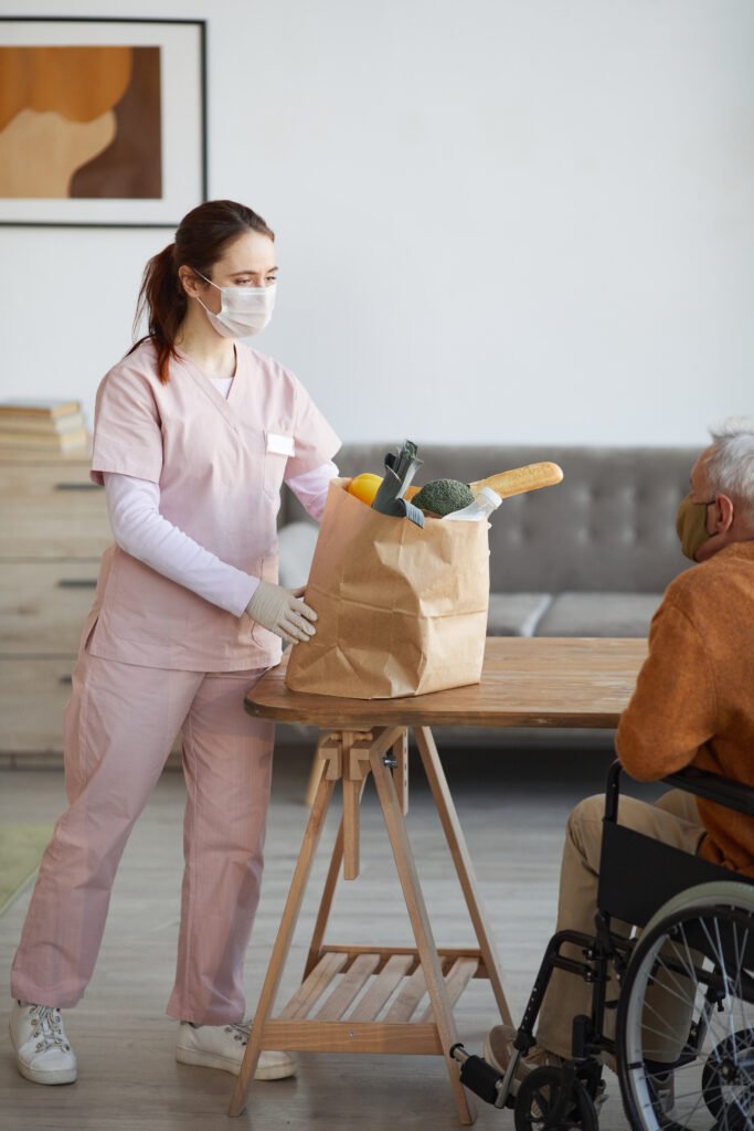 Betreuungskraft bringt Lebensmittel für eine Haushaltshilfe zu einem Senior nach Hause