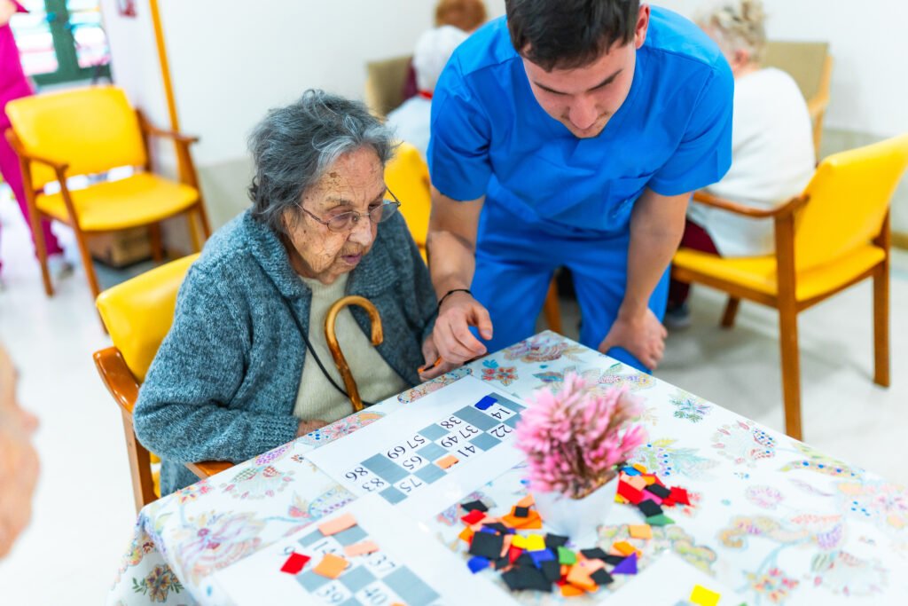 Betreuungskraft unterstützt eine Seniorin bei einem Gesellschaftsspiel zur kognitiven Aktivierung